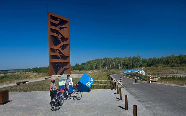 Radfahrer an der Landmarke Rostiger Nagel am Sedlitzer See