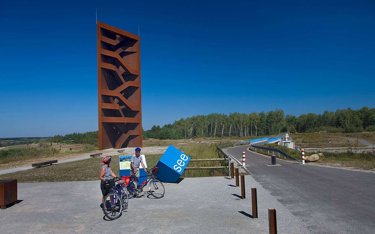Radfahrer an der Landmarke Rostiger Nagel am Sedlitzer See